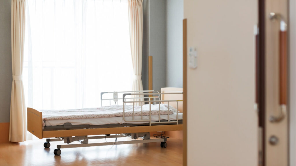 Cama com grade de proteção lateral em quarto iluminado, adaptado para idosos.
