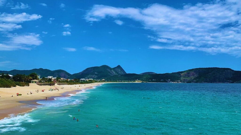 Vista da Praia de Camboinhas, em Niterói, com mar limpo e calmo, areia clara e cenário tranquilo.