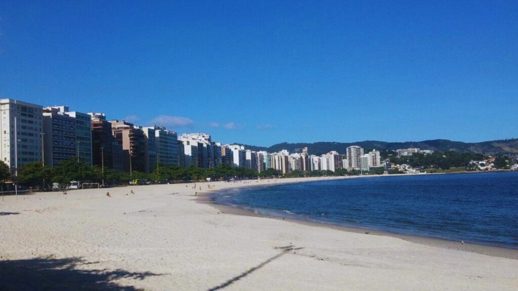 Praia de Icaraí em Niterói, com calçadão amplo, mar calmo e prédios ao fundo, ideal para caminhadas e lazer de idosos